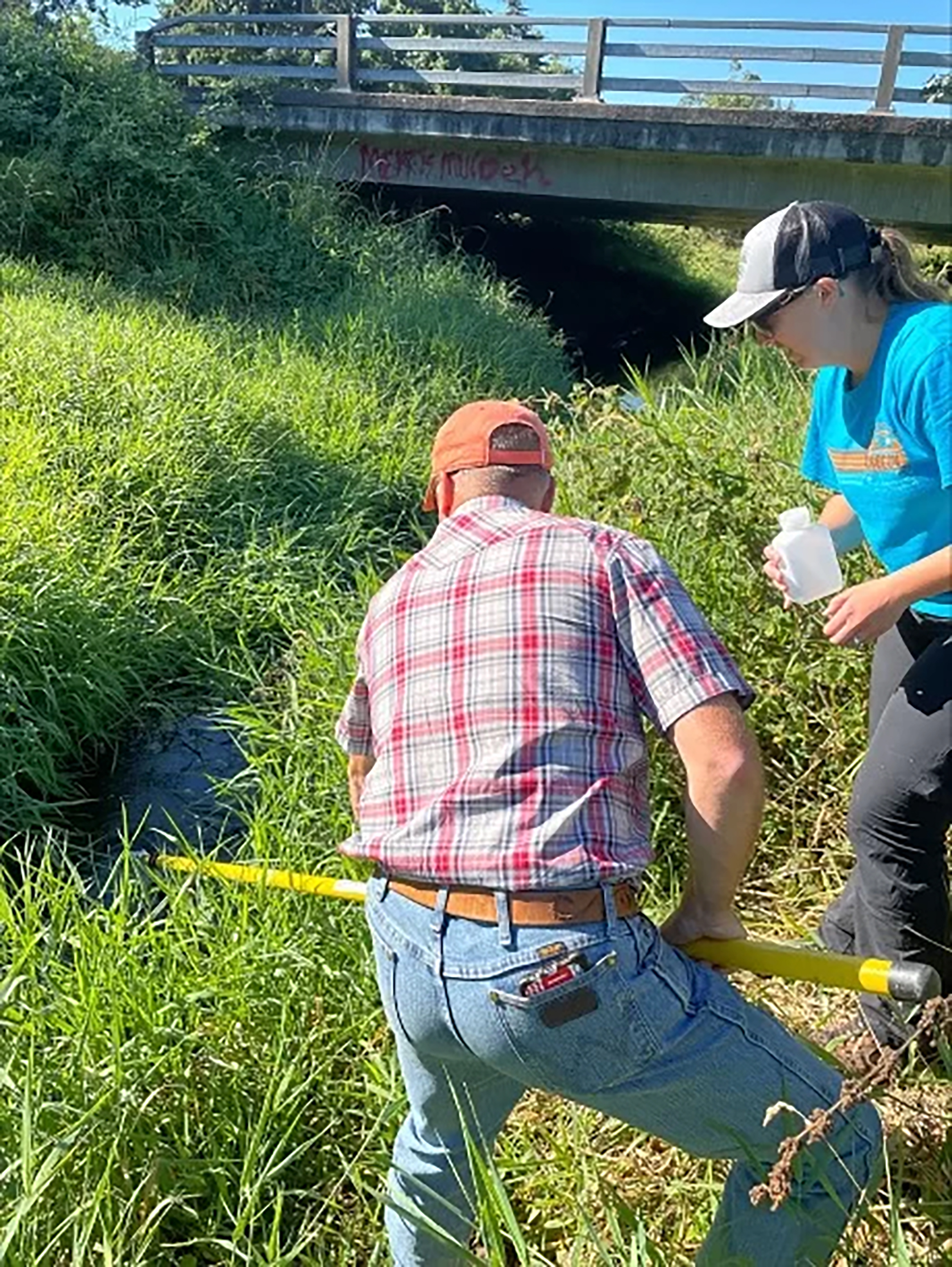 Rifenburg holds a water sample beside a stream.