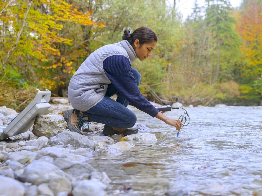 Side view of young female biologist using multiparameter instrument while testing dissolved oxygen in river.
