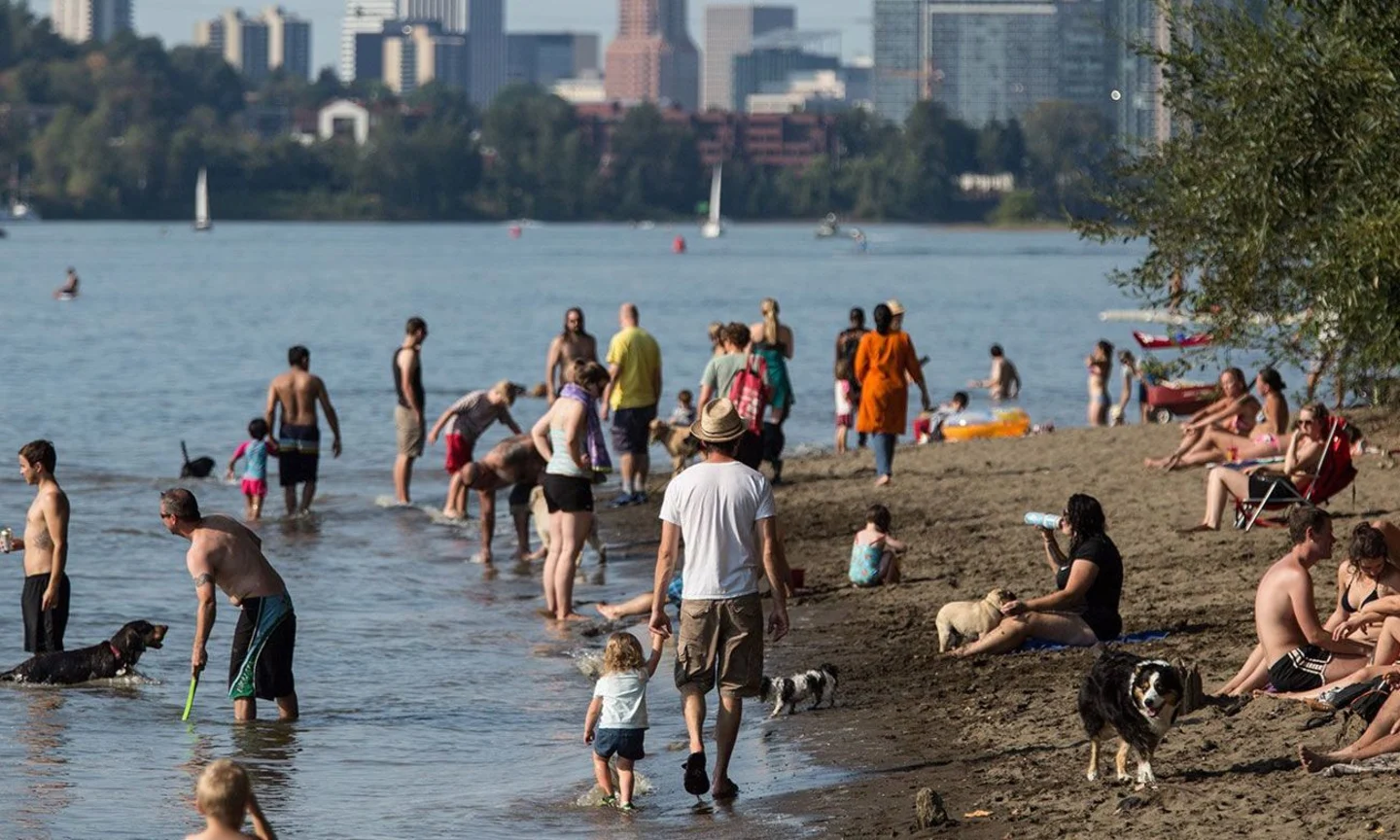 Swimmers and beach-goers along the Willamette River in Portland, OR with the skyline of downtown in the background.